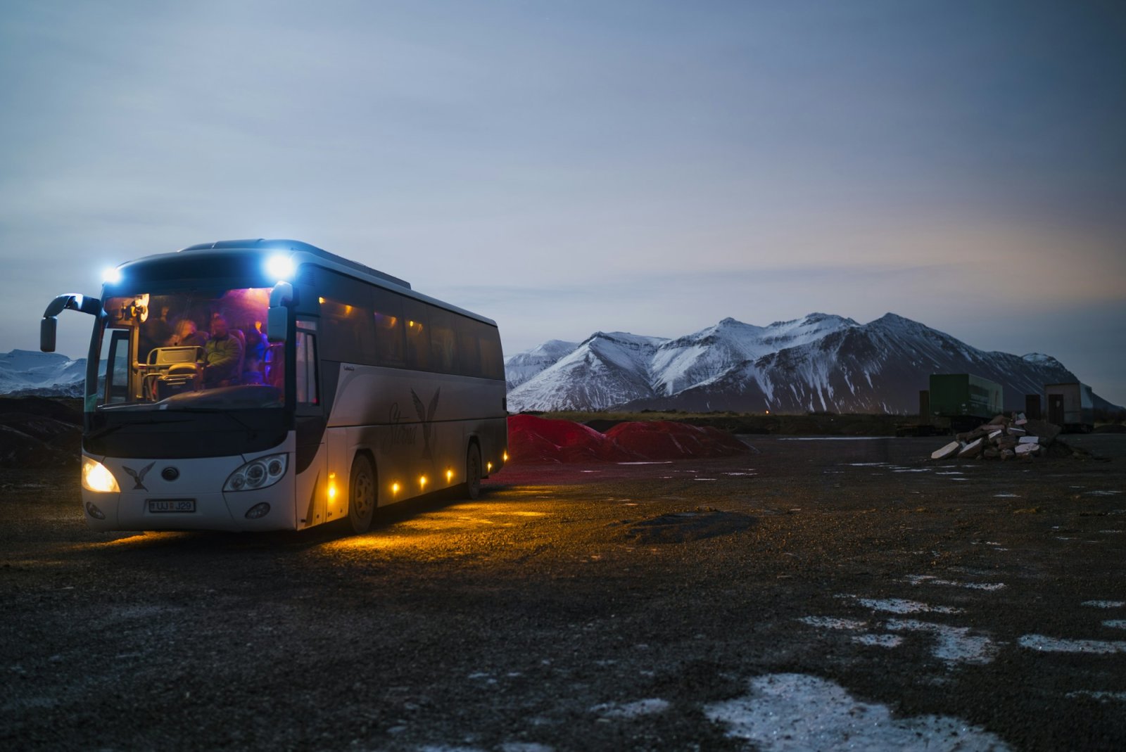 Full-size motor coach parked at dusk with mountains behind